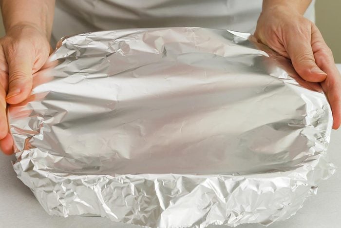 Chef wraps baking pan with aluminum foil.