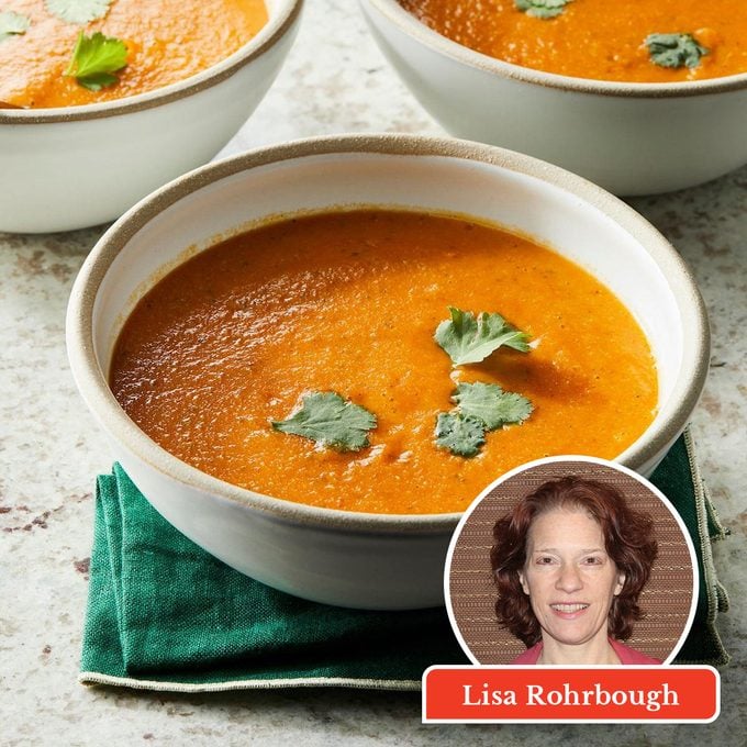 A bowl of orange soup garnished with cilantro leaves sits on a green napkin. Two more bowls are partially visible. Inset is a headshot of a woman labeled “Lisa Rohrbough.”.