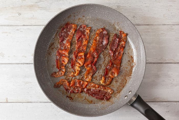 Bacon strips being cooked in large skillet pan