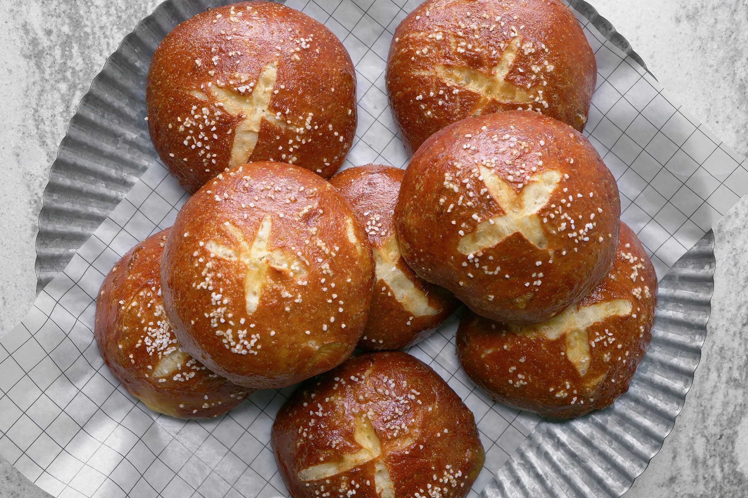 Pretzel buns on paper which is placed on a plate on counter.
